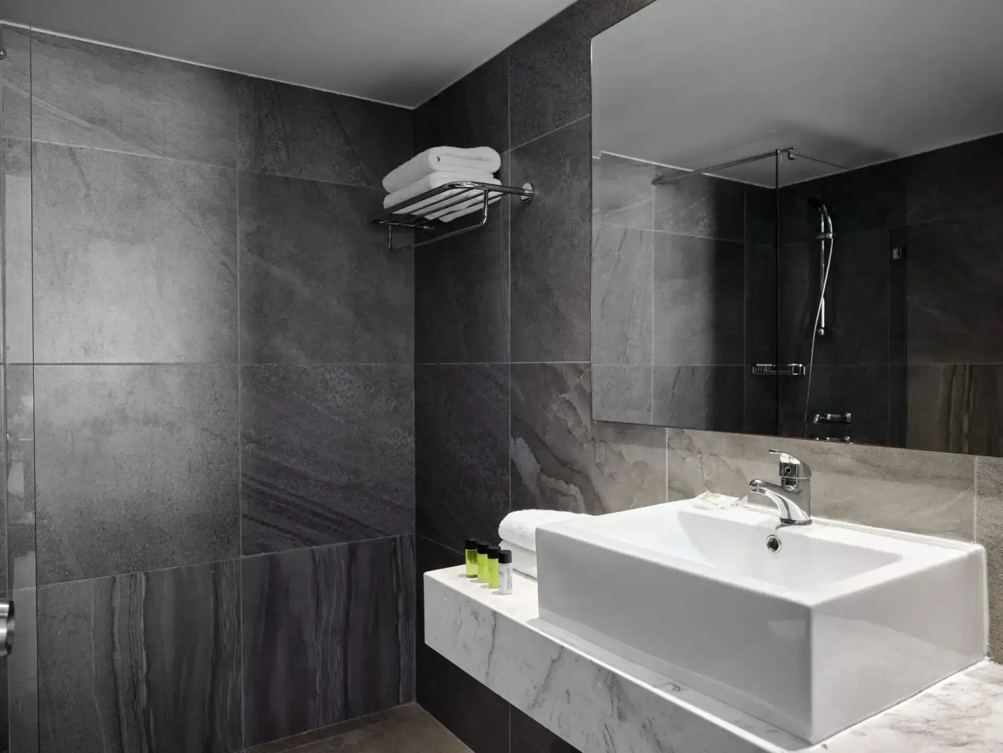Modernes Badezimmer mit dunkelgrauen Fliesen, weißem Waschbecken und großem Wandspiegel.