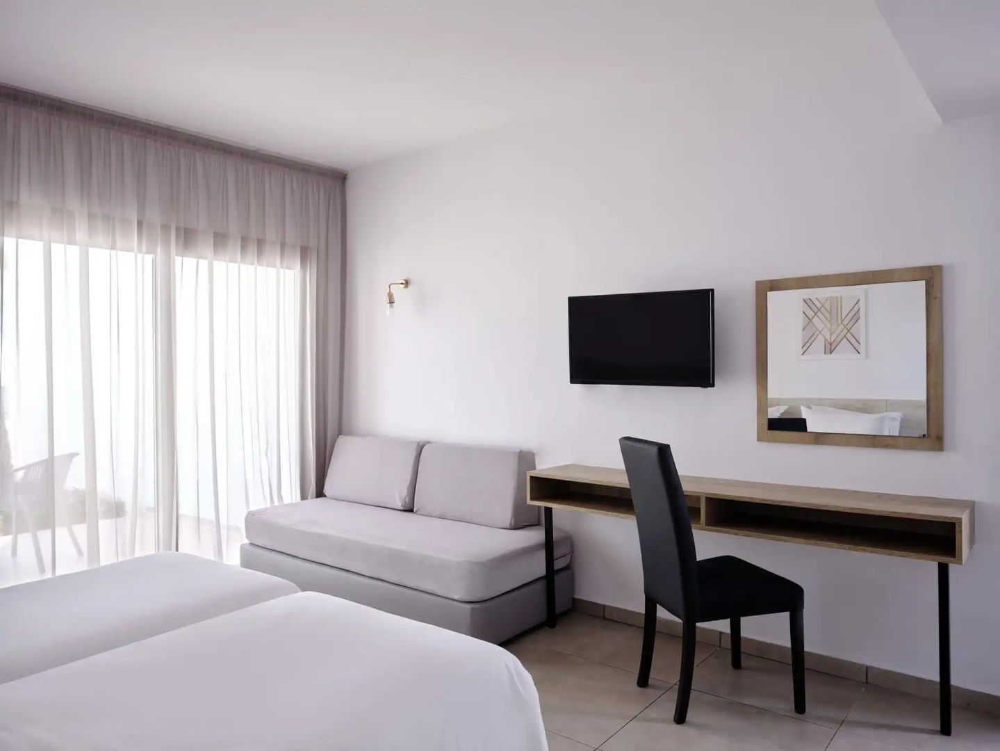 Hell eingerichtetes Hotelzimmer mit Betten, Schlafsofa, Schreibtisch und Wandfernseher.