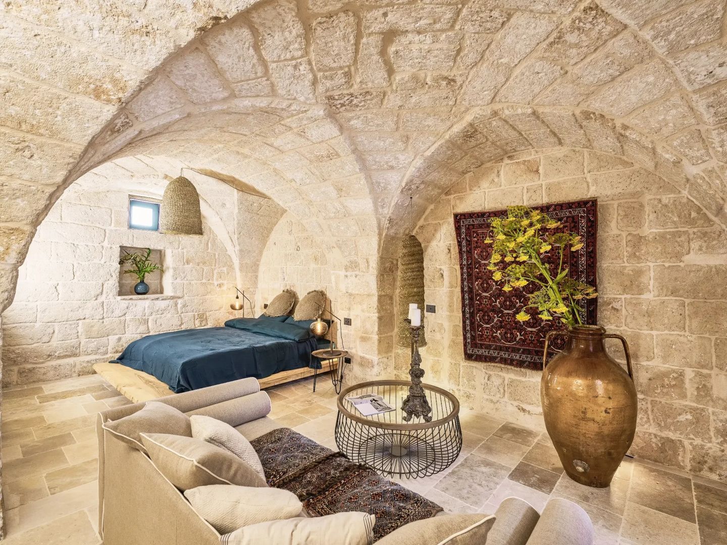 Schlafzimmer mit Kreuzgewölbe aus Naturstein, blauem Bett und Sitzbereich.