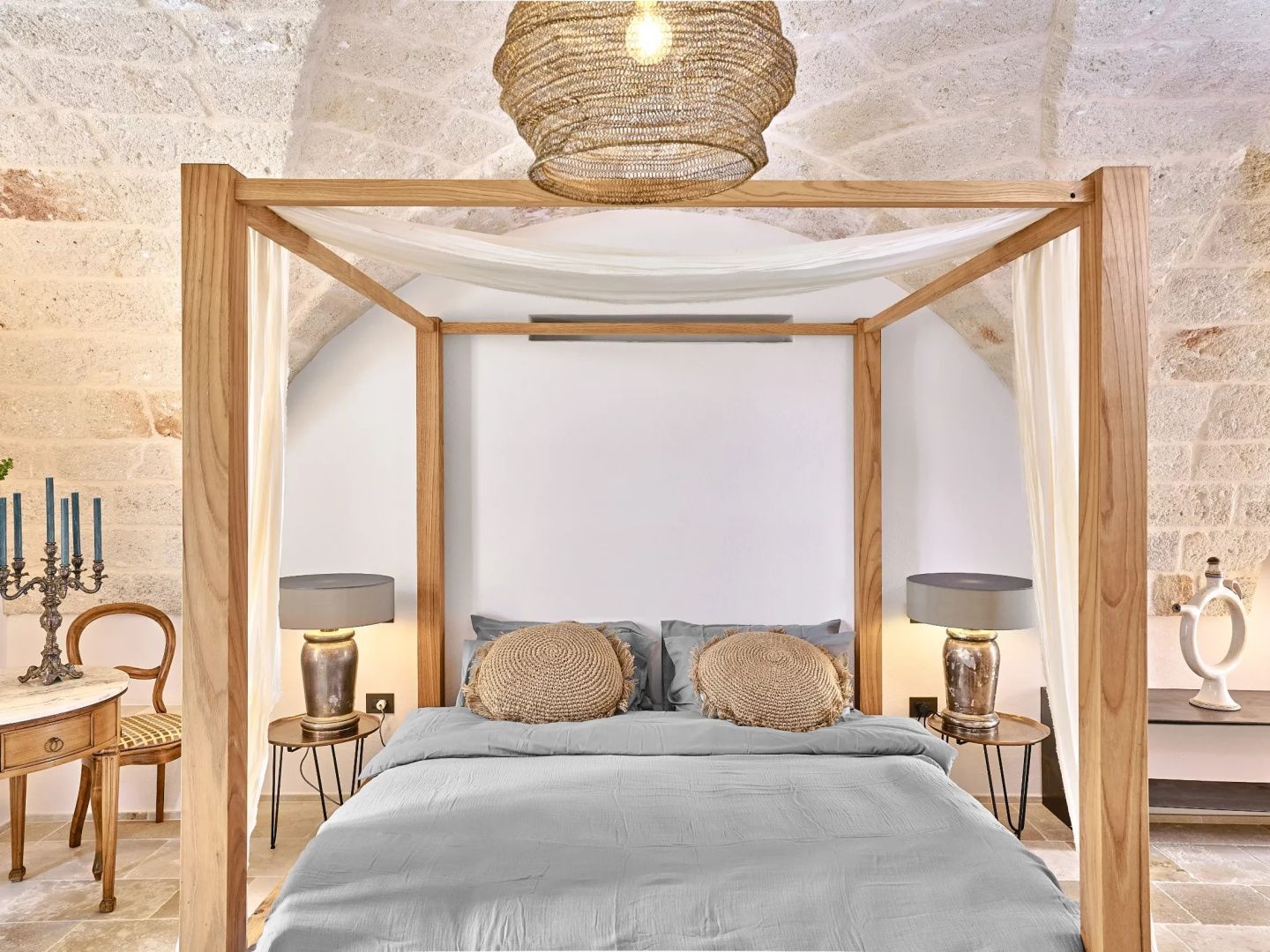 Himmelbett aus Holz mit hellgrauer Bettwäsche unter einer gewölbten Steindecke.