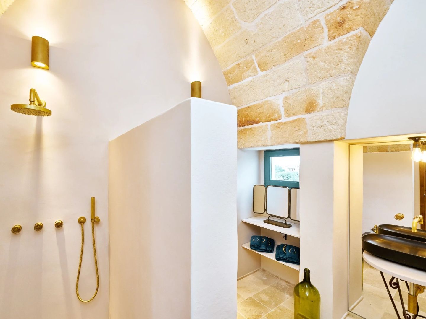 Modernes Badezimmer mit goldener Armatur, weißer Wand und Natursteingewölbe an der Decke.