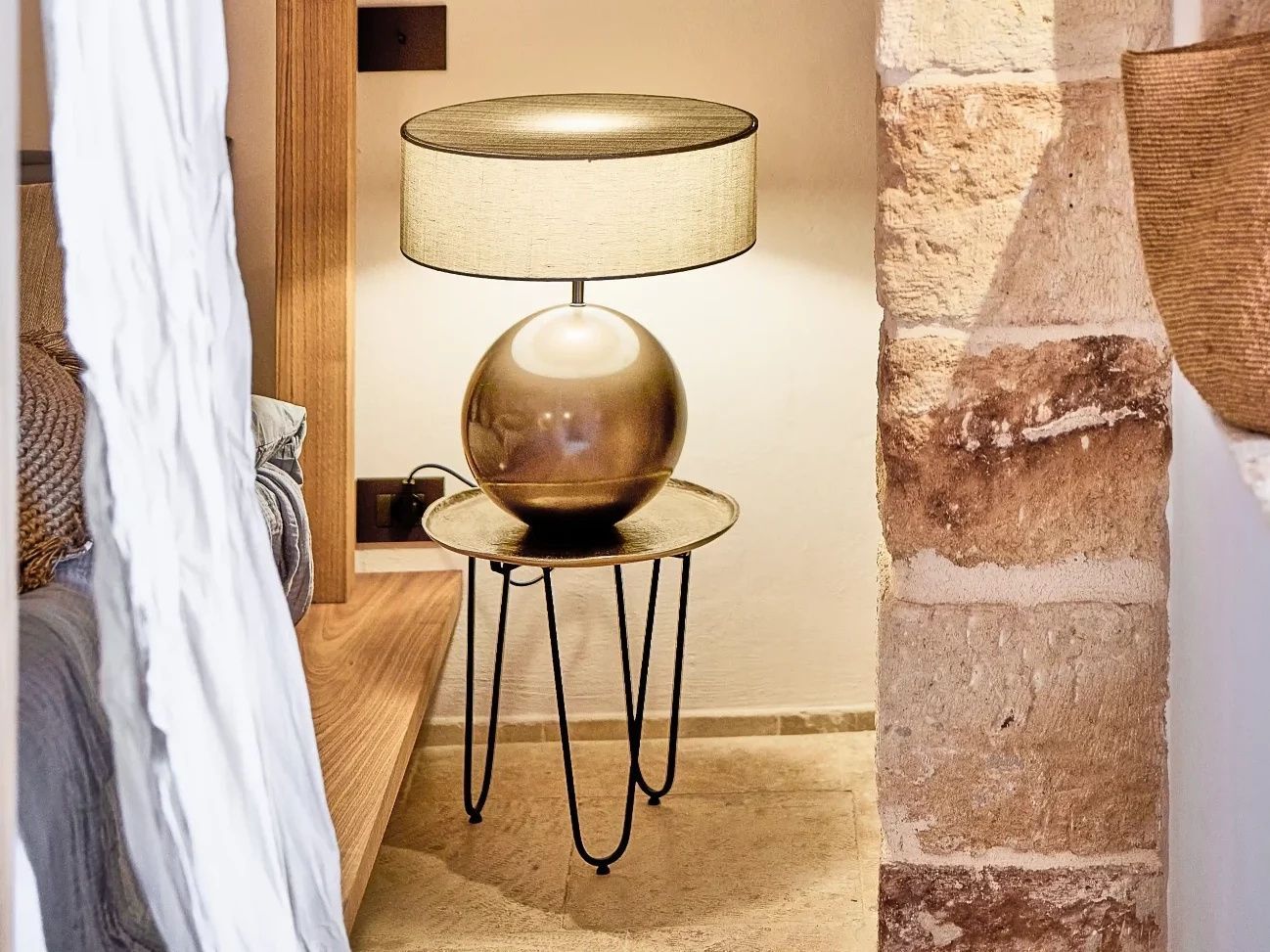 Moderne Nachttischlampe mit kugelförmigem Fuß neben einer sichtbaren Natursteinwand.