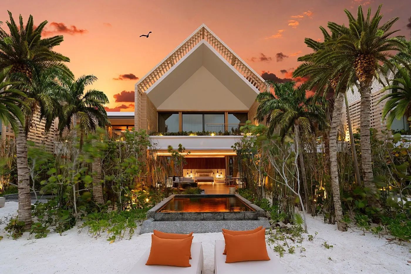 Eine zweistöckige Villa am Strand mit spitzem Dach, eigenem Pool und zwei Sonnenliegen.