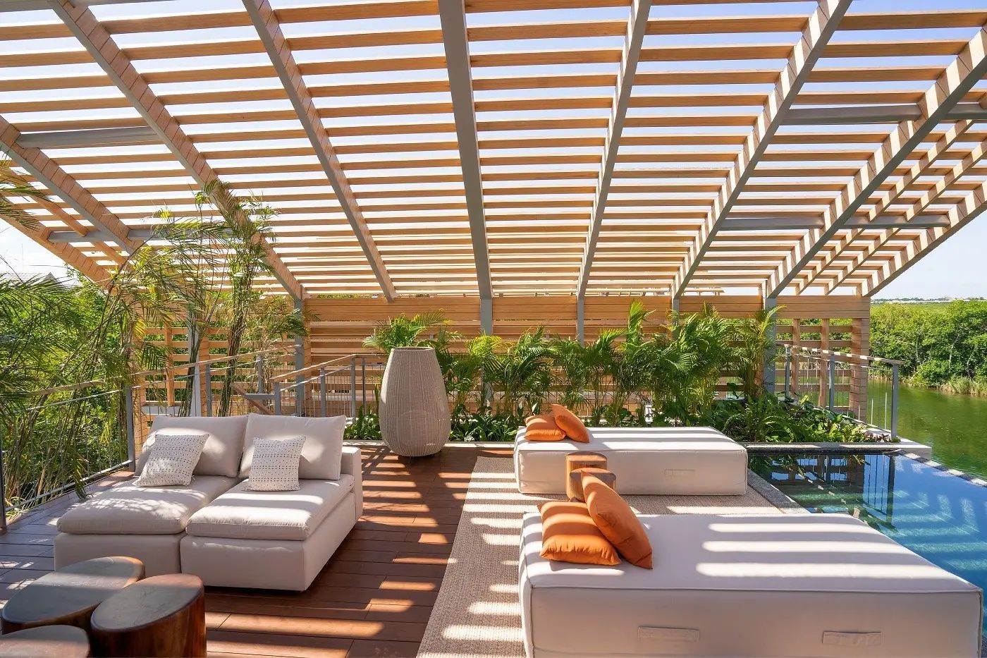 Überdachte Terrasse mit Holzpergola, Loungemöbeln sowie Liegen mit orangefarbenen Kissen.