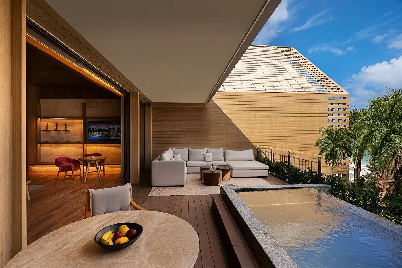 Terrasse mit Ecksofa, kleinem Pool und Tisch mit Obstschale vor einer Holzfassade.
