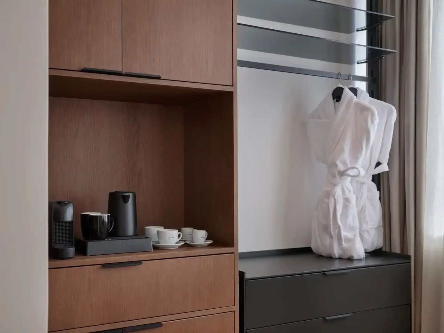 Holzschrank mit Kaffeemaschine, Wasserkocher und Tassen sowie ein weißer Bademantel.