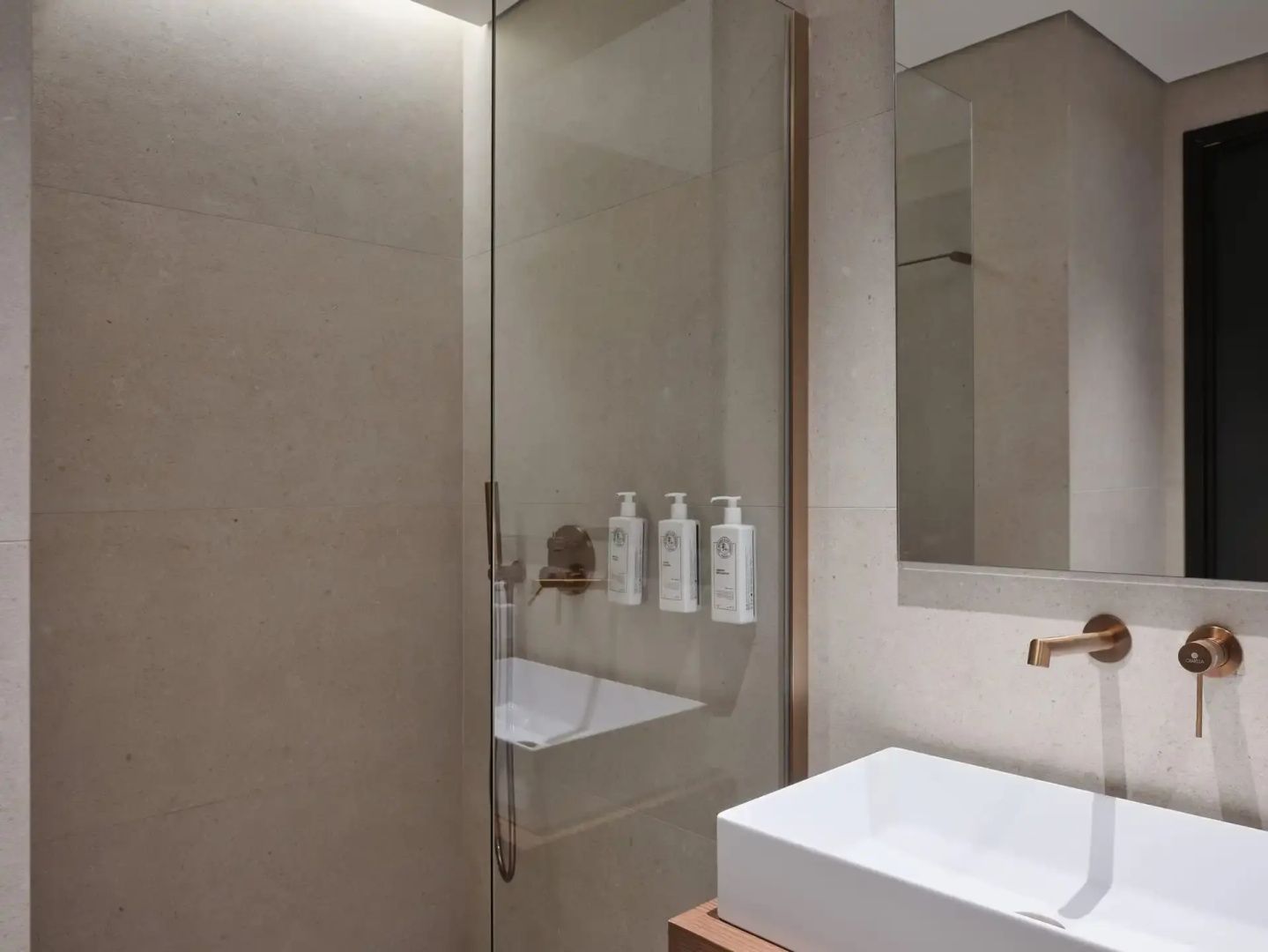 Badezimmer mit weißem Waschtisch, Spiegel und gläserner Duschabtrennung