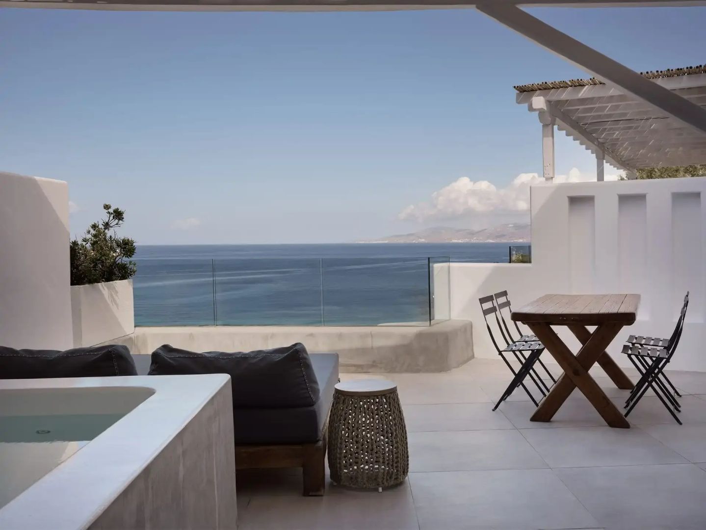 Terrasse mit Holztisch, Sitzgelegenheiten und freiem Blick auf das blaue Meer.