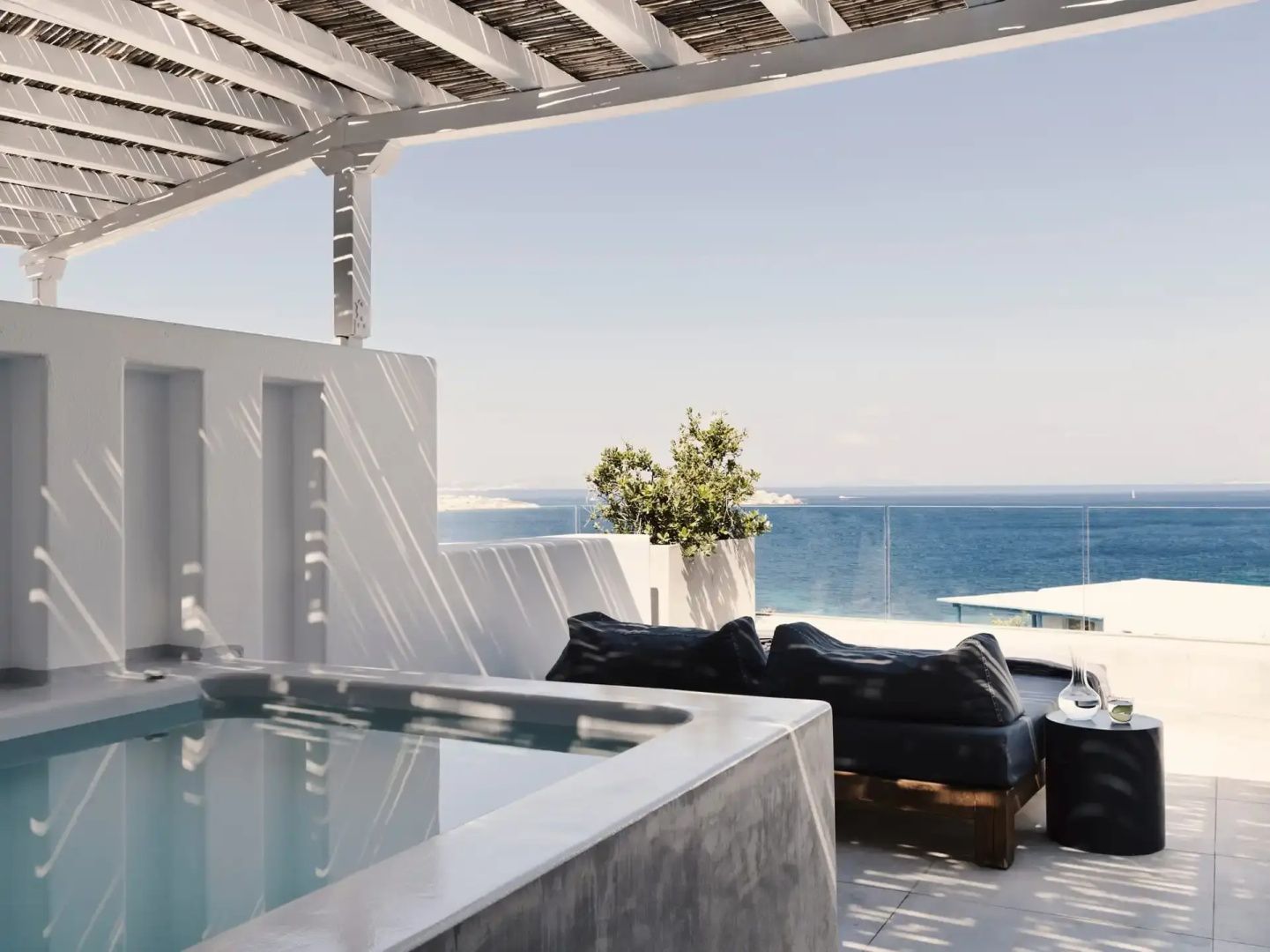 Terrasse mit Whirlpool, bequemen Sitzkissen und unverbautem Meerblick unter einer Pergola.