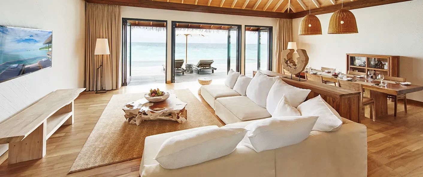 Helles Wohnzimmer mit großem Ecksofa, Holztisch und geöffneter Front zur Terrasse am Strand.