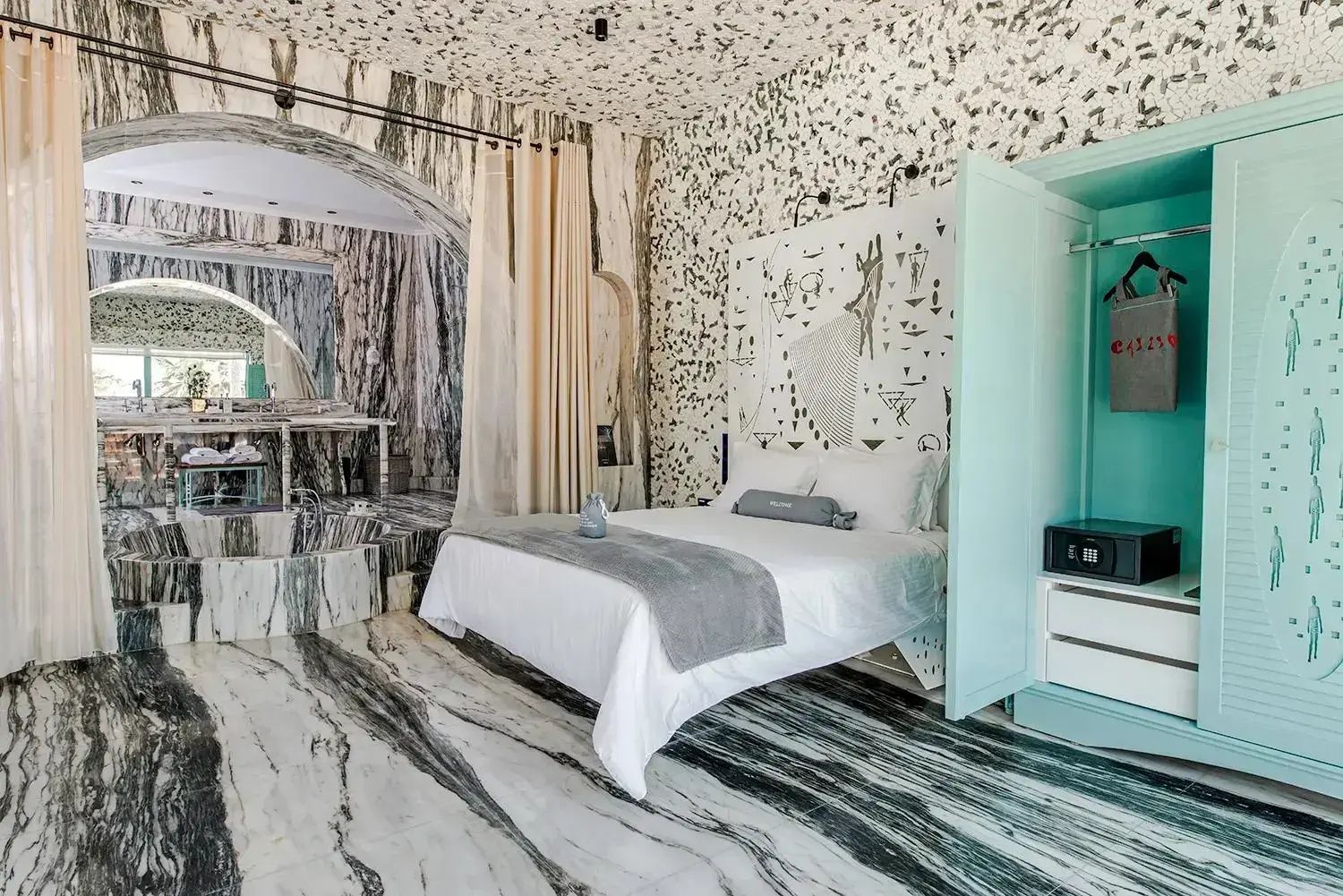 Hotelzimmer mit weiß bezogenem Doppelbett, Marmorboden und kunstvoll gestalteter Wand hinter dem Bett.