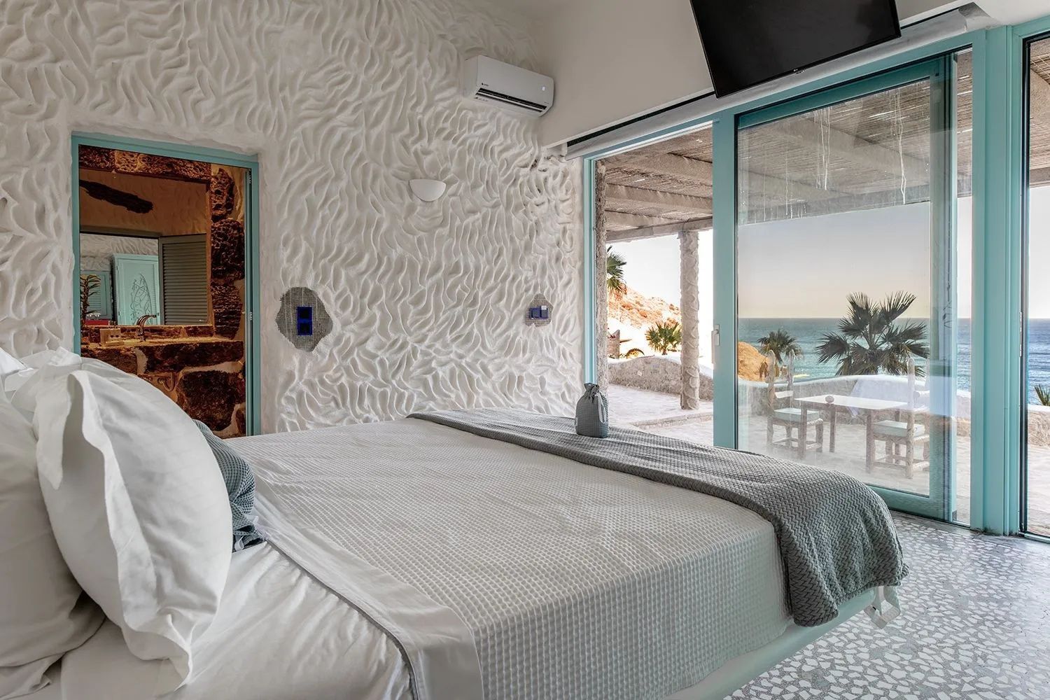 Blick vom Schlafzimmer durch die Glasfront auf eine Terrasse mit Meerblick.