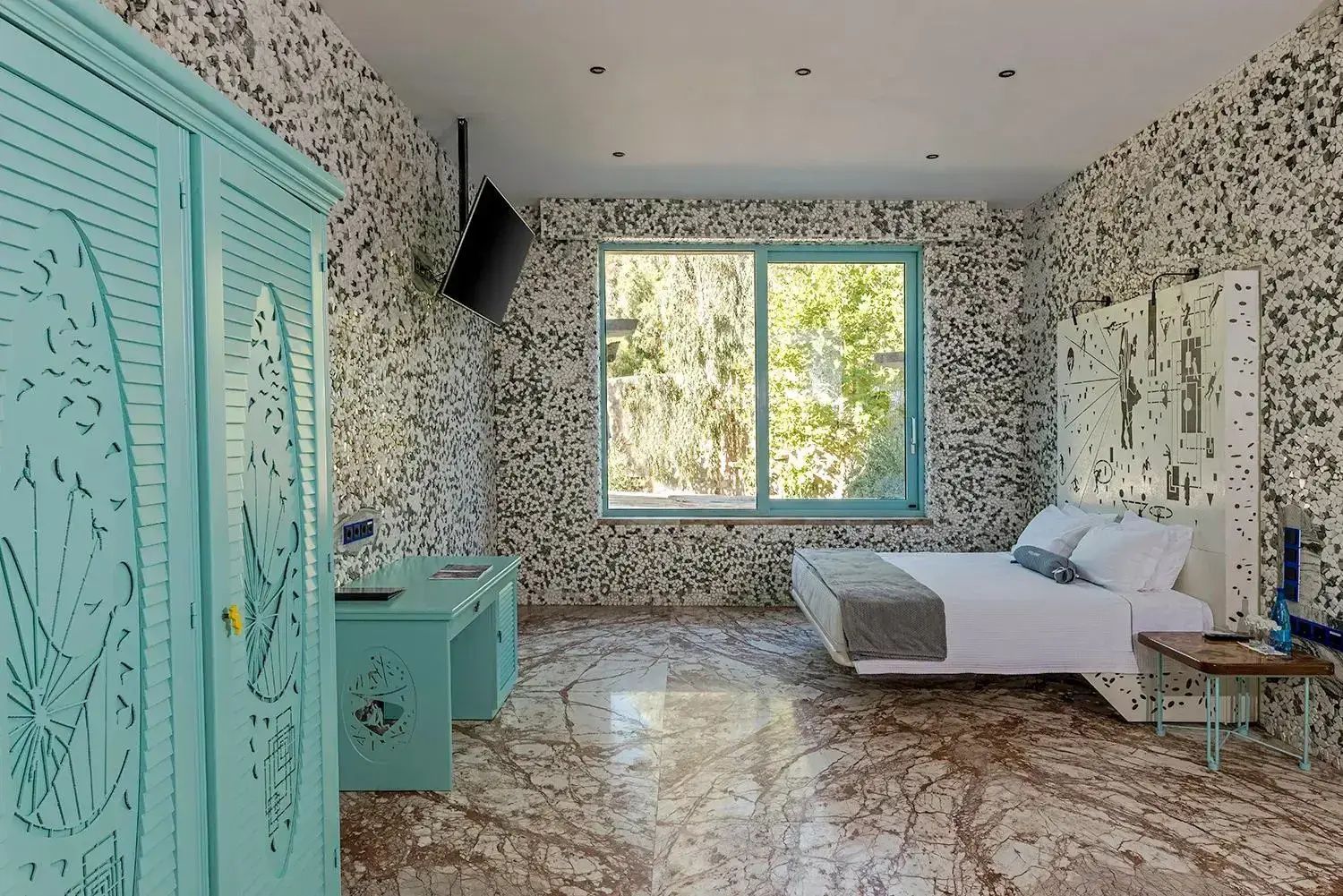 Schlafbereich mit türkisblauem Schrank, hellen Mosaikwänden und braunem Marmorboden.