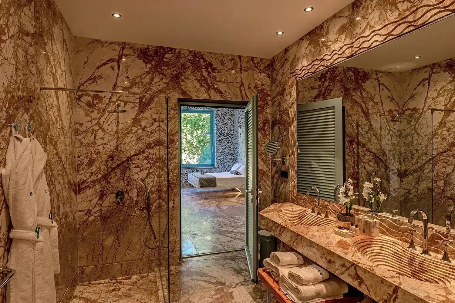 Badezimmer aus braun gemustertem Marmor mit Waschtisch, Dusche und offenem Durchgang.