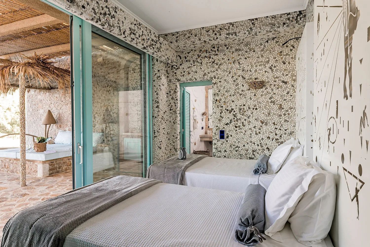Zwei Betten in einem Hotelzimmer mit Steinmosaik und großen Glasfenstern.