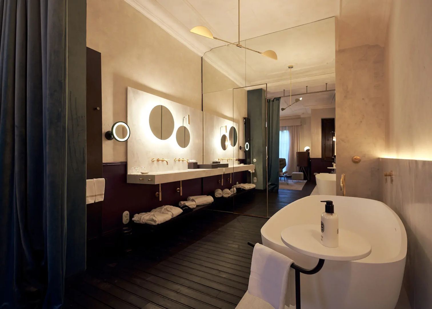 Badezimmer mit Doppelwaschtisch, beleuchteten Rundspiegeln und freistehender Badewanne.