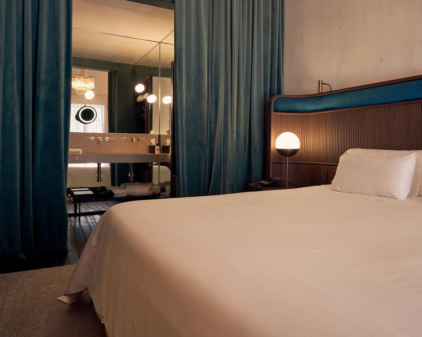Doppelbett mit blauem Kopfteil und Durchblick zum Badezimmer hinter blauen Vorhängen.