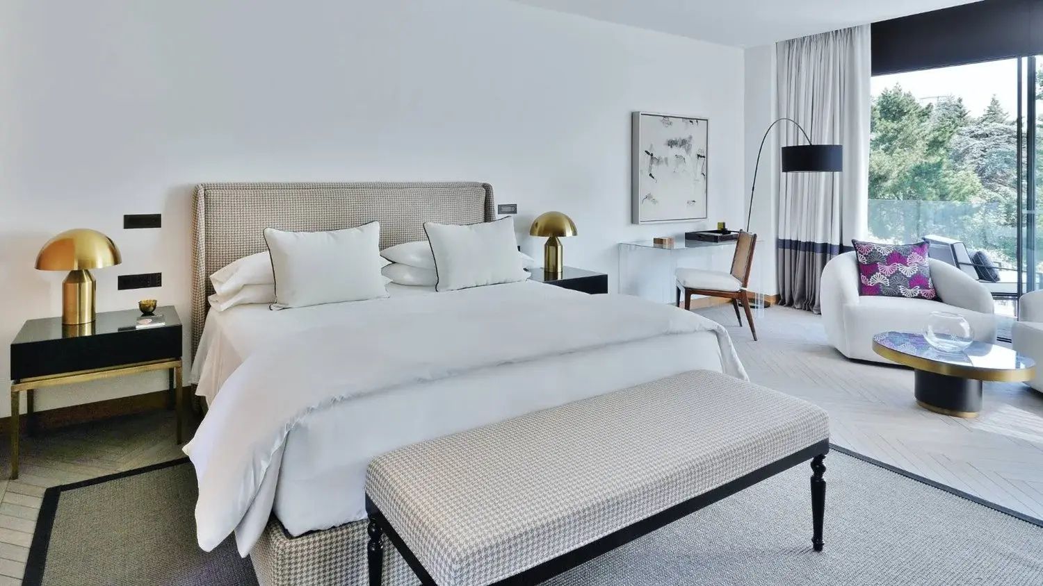 Hell eingerichtetes Hotelzimmer mit Doppelbett, Bettbank, Schreibtisch und Stehlampe.