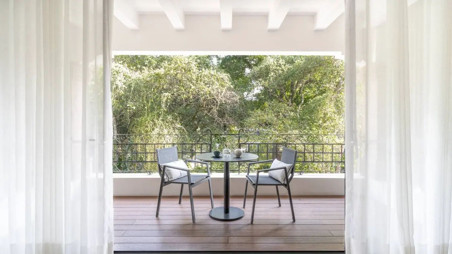 Balkon mit zwei Stühlen und einem kleinen Tisch mit Blick auf grüne Bäume.