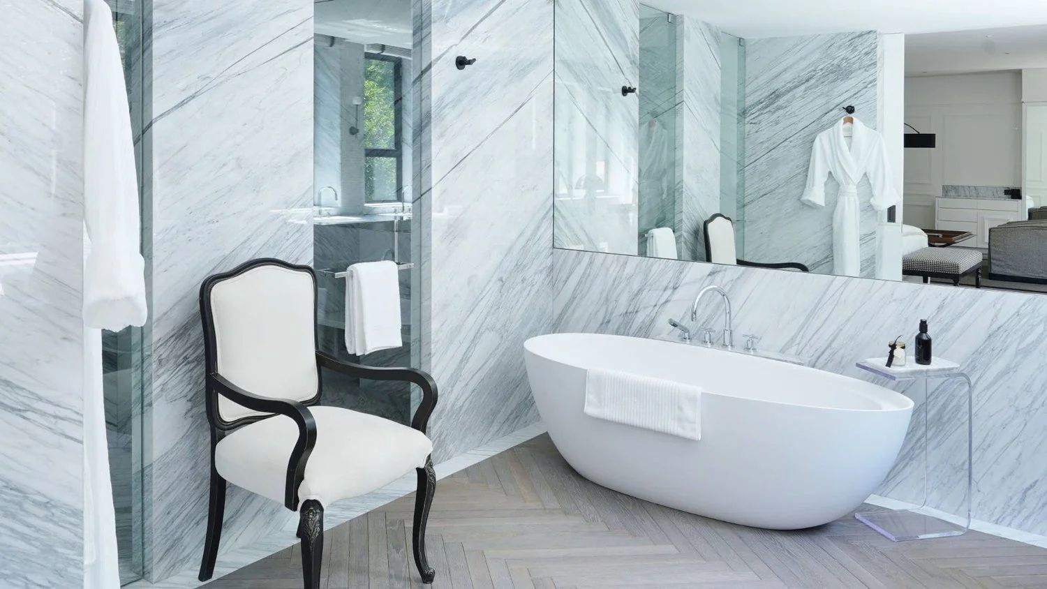 Marmoriertes Badezimmer mit freistehender Badewanne und Stuhl aus Holz.