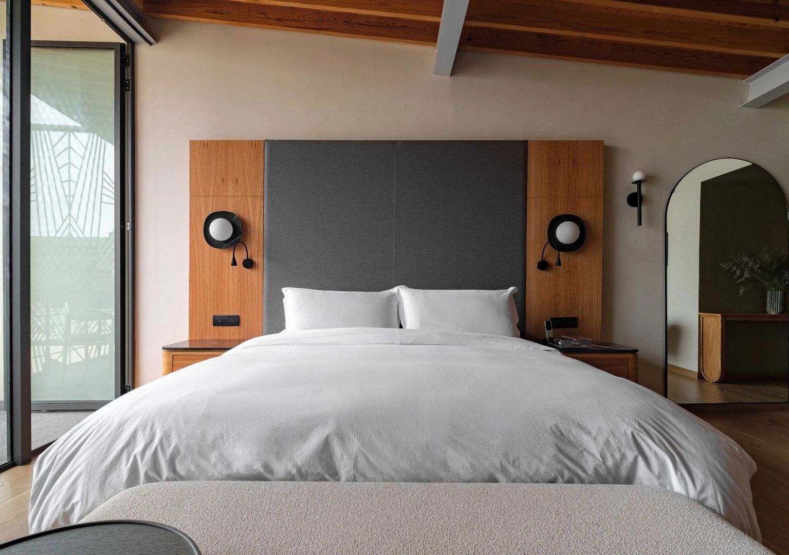 Großes Doppelbett mit weißer Bettwäsche, grauem Kopfteil und seitlichen Wandleuchten.