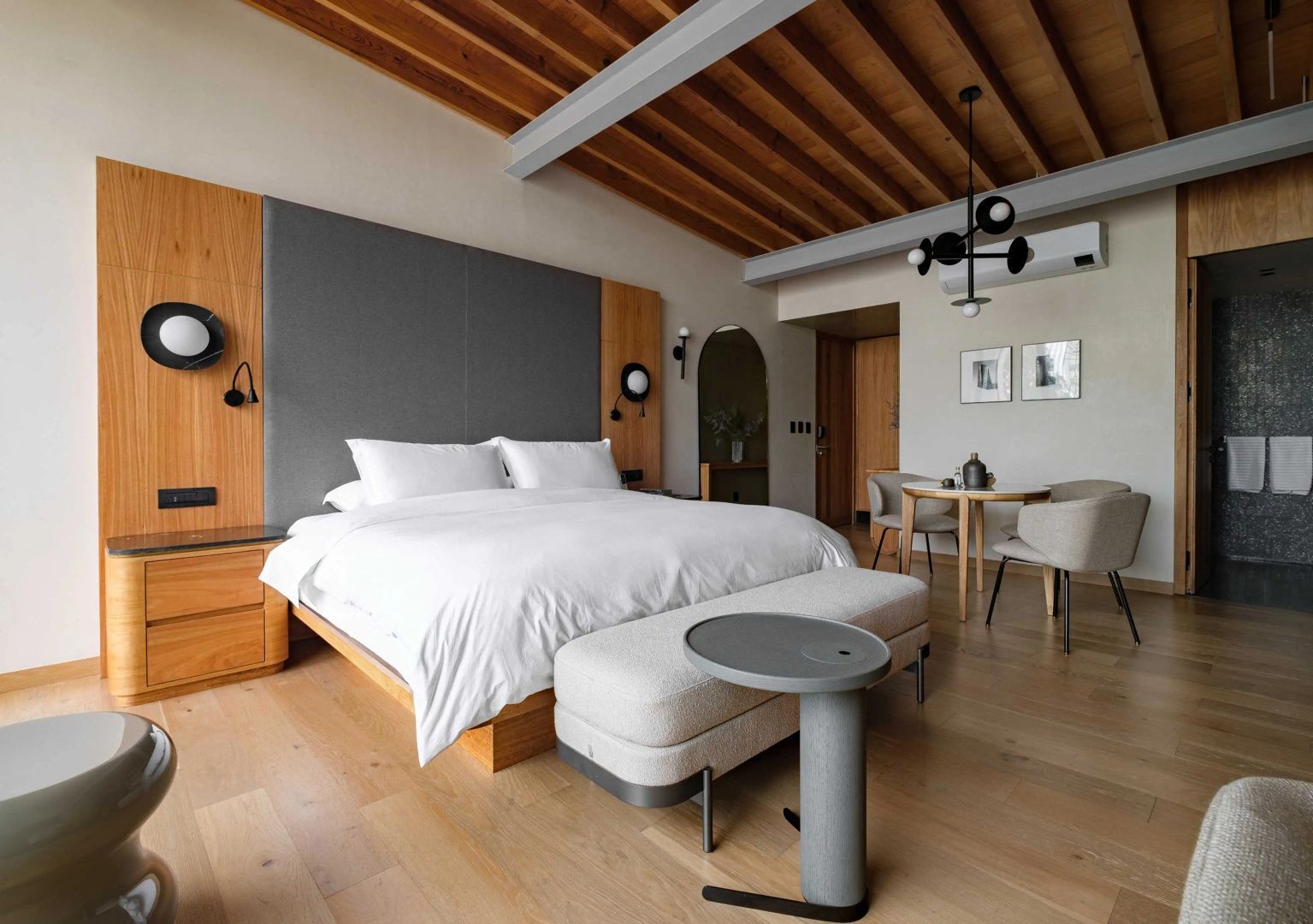 Schlafbereich mit Doppelbett, gepolsterter Bank und kleinem Esstisch mit Stühlen.