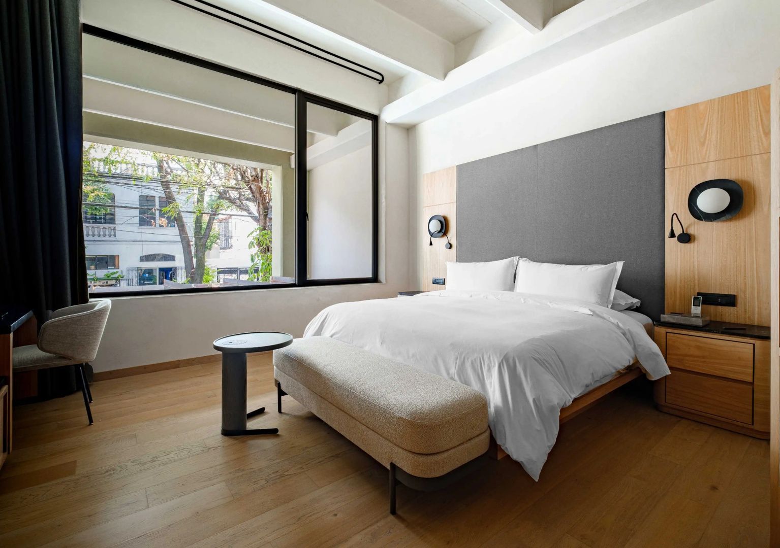 Doppelbett vor großem Fenster mit Blick auf Bäume und die gegenüberliegenden Gebäude.