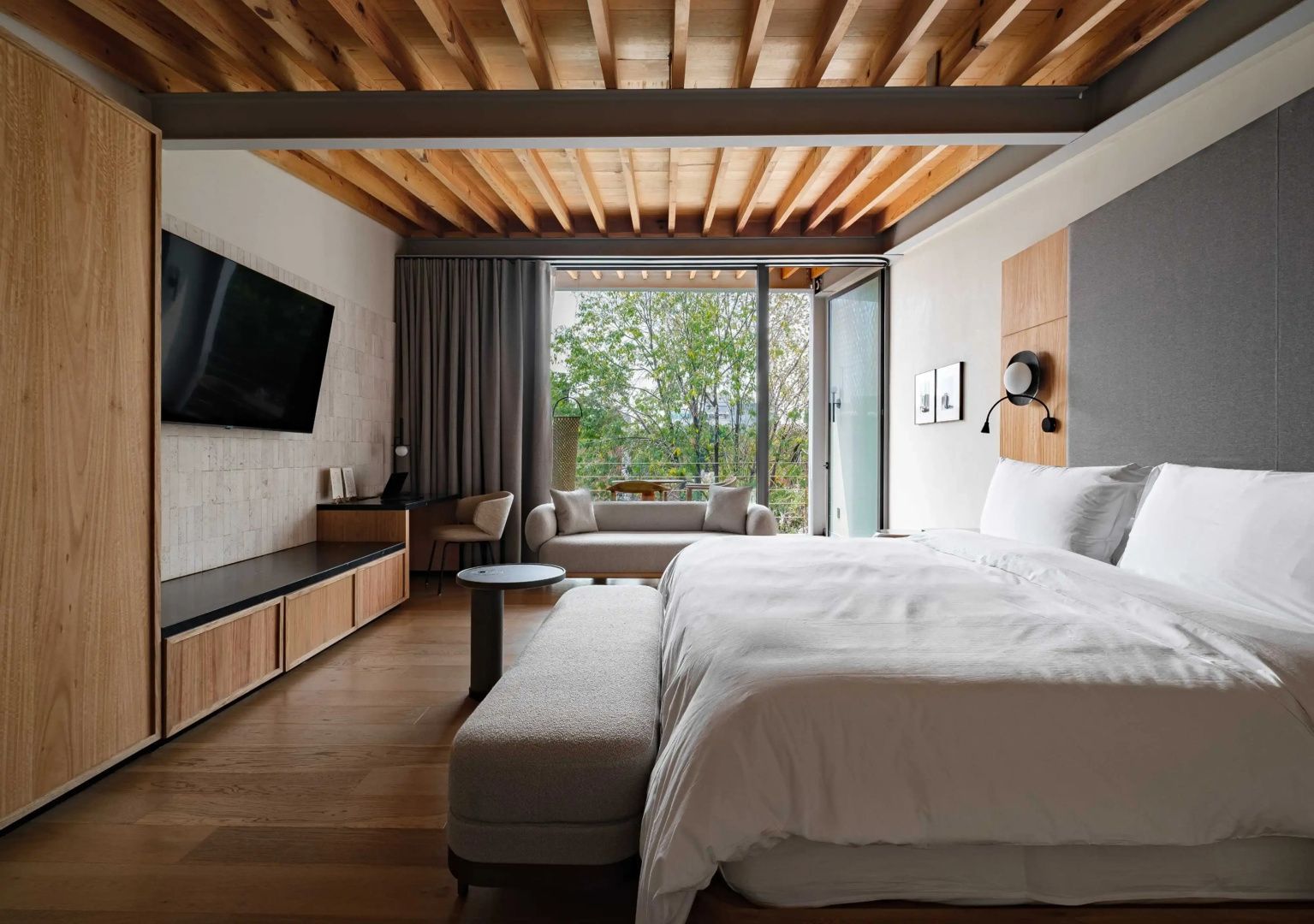 Modernes Hotelzimmer mit Holzdecke, großem Bett, Sofa und Zugang zum Balkon.