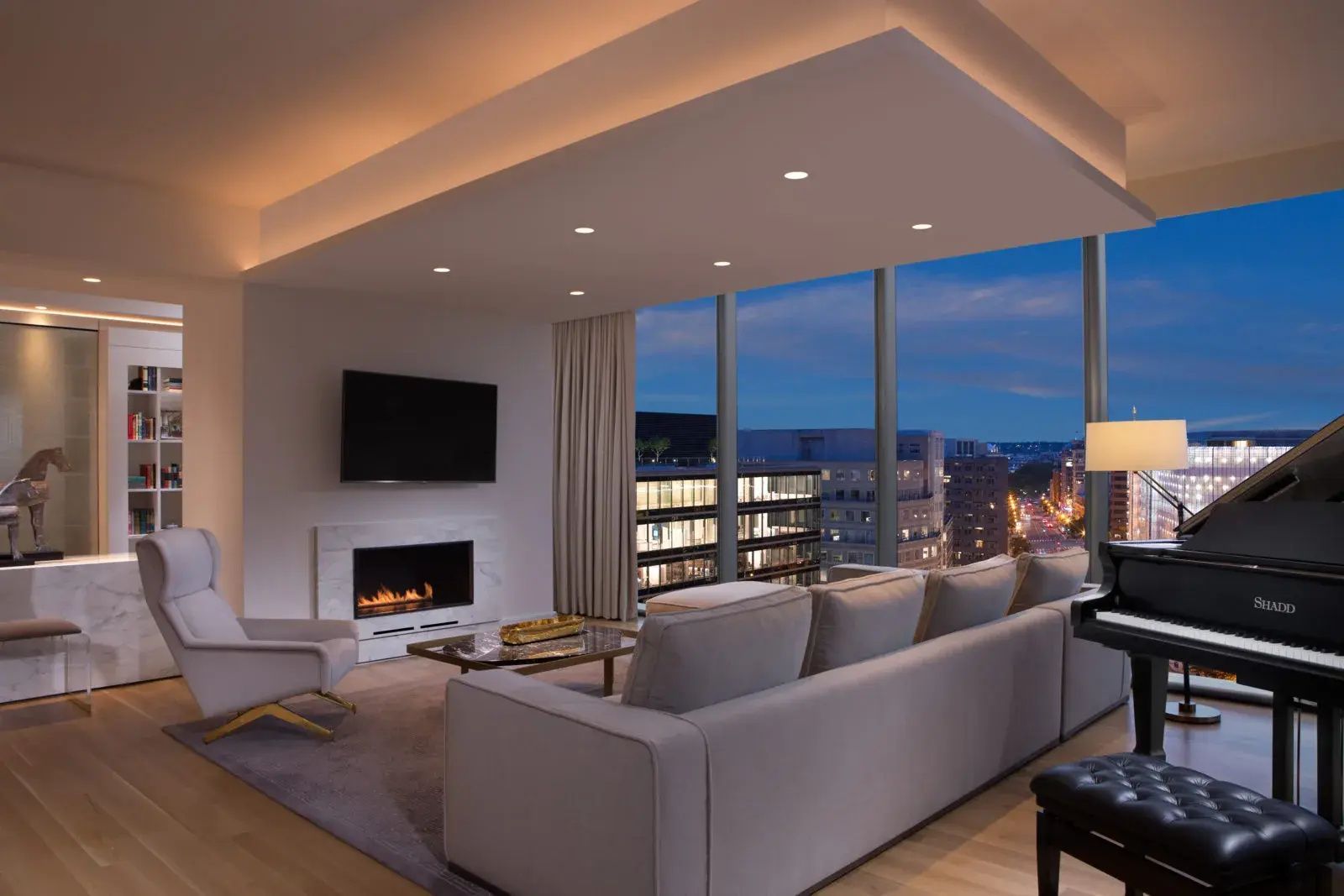 Modernes Wohnzimmer einer Suite mit grauem Sofa, Kamin und großen Fenstern mit Stadtblick.