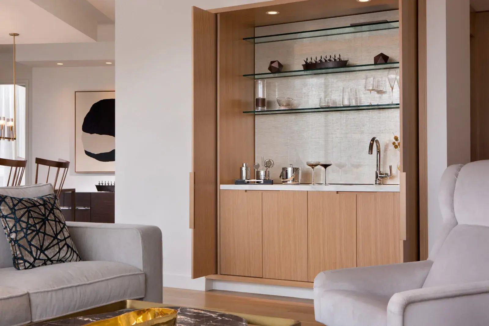 Geöffnete Bar im Holzschrank mit Gläsern, Cocktail-Set und Waschbecken im Wohnbereich.