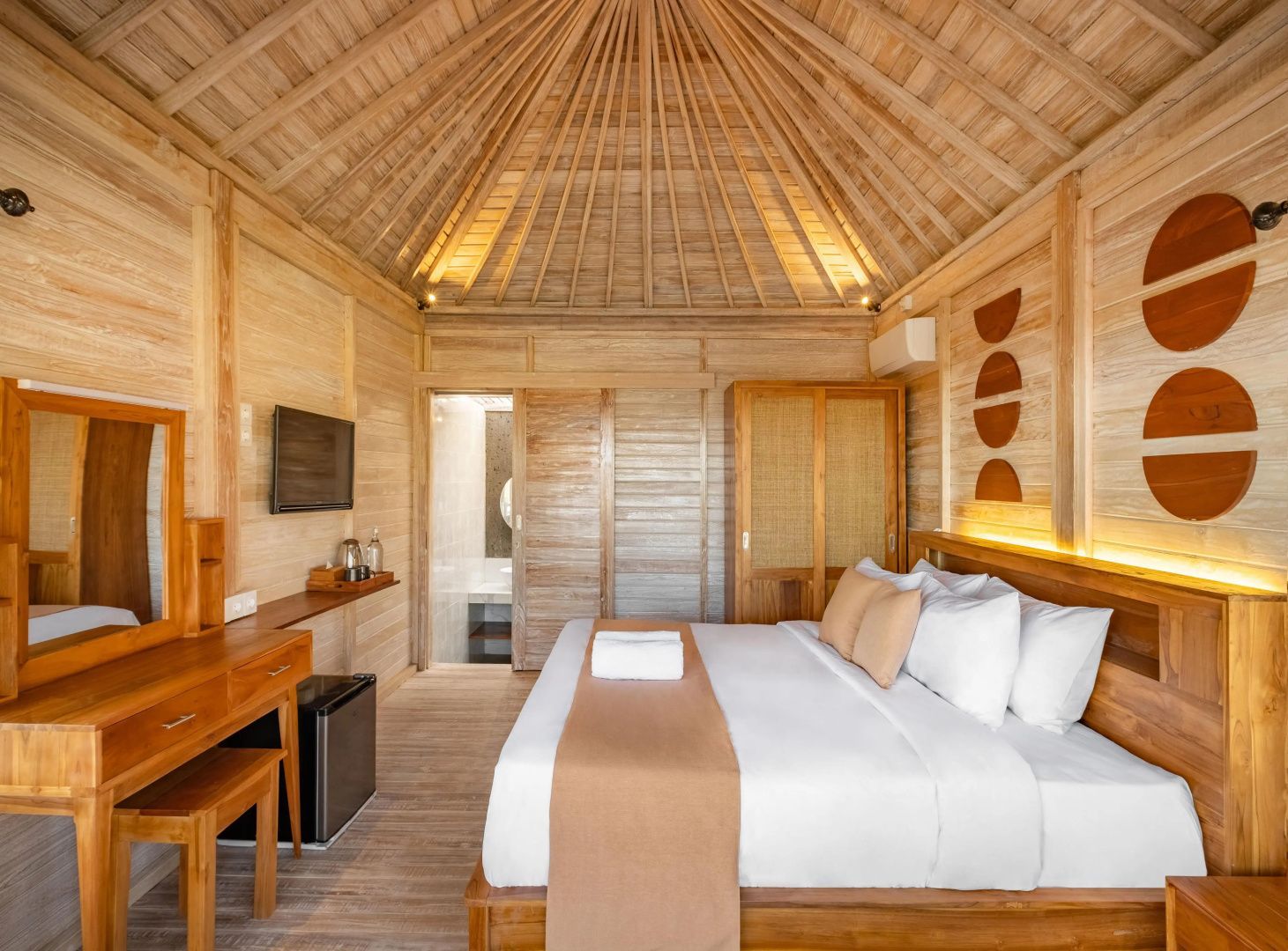 Helles Holzschlafzimmer in einem Bungalow mit großem Doppelbett und hoher Holzdecke.