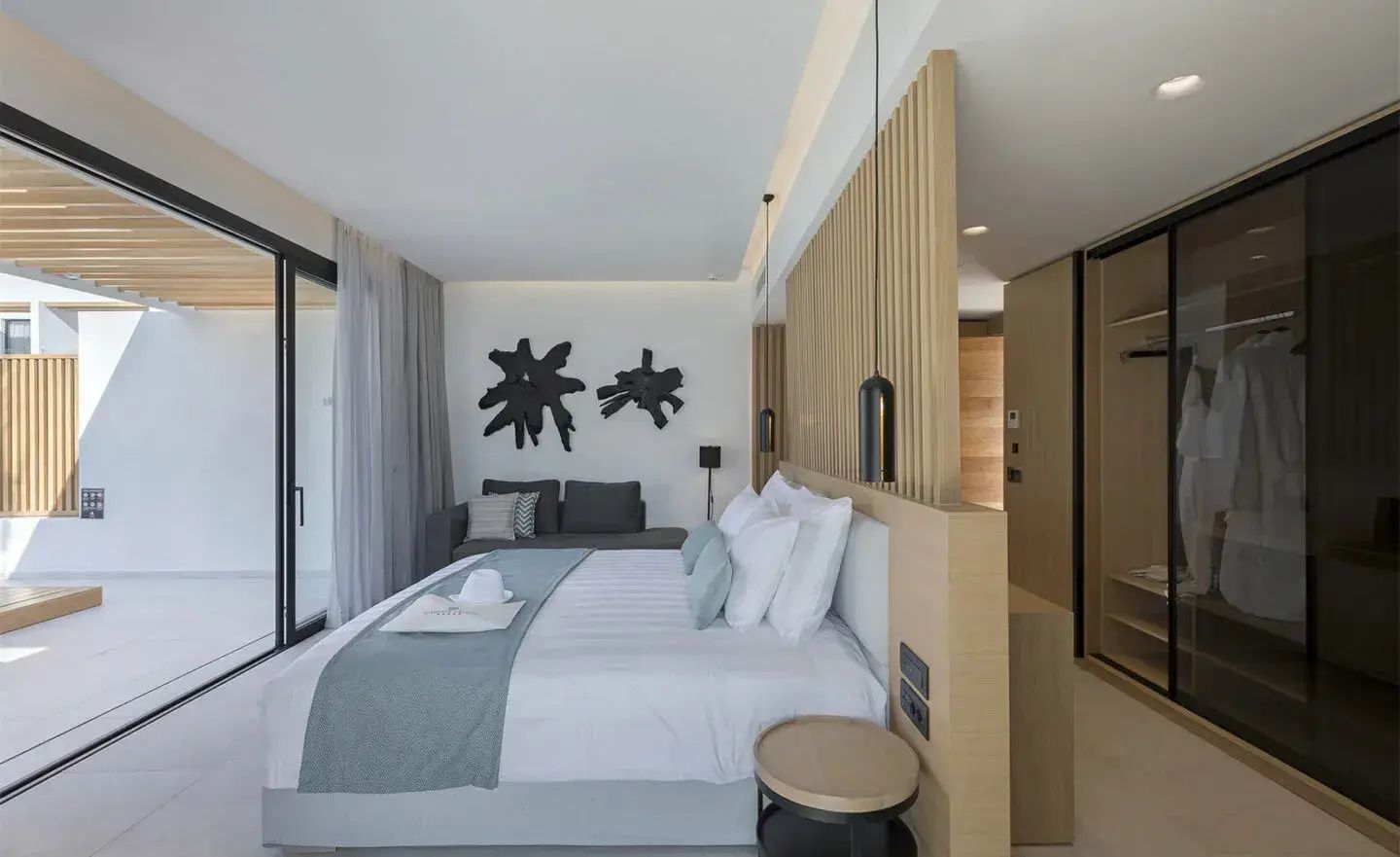 Helles Schlafzimmer einer Suite mit Doppelbett, Raumteiler aus Holz und gemütlicher Sitzecke.