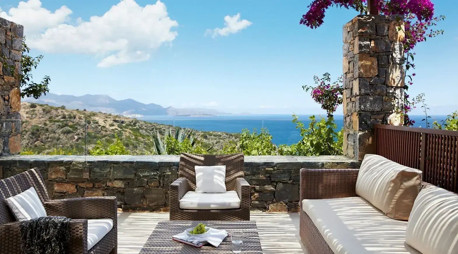 Möblierte Terrasse mit Rattanmöbeln, Steinmauer und Panoramablick auf das Meer.