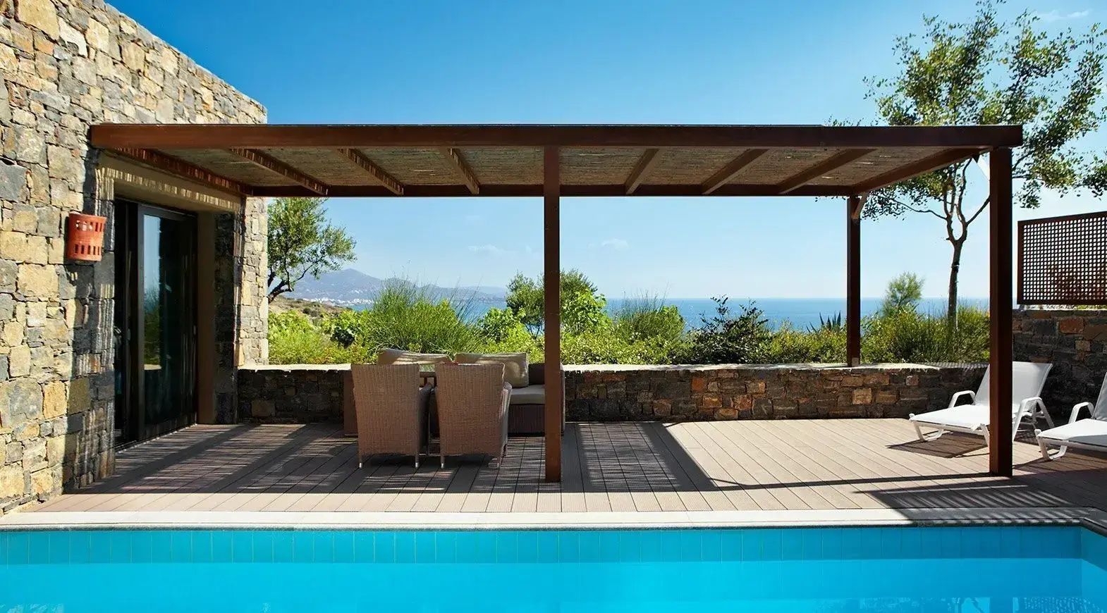 Überdachte Terrasse mit Holzpergola, gemütlichen Sitzmöbeln und einem blauen Pool.