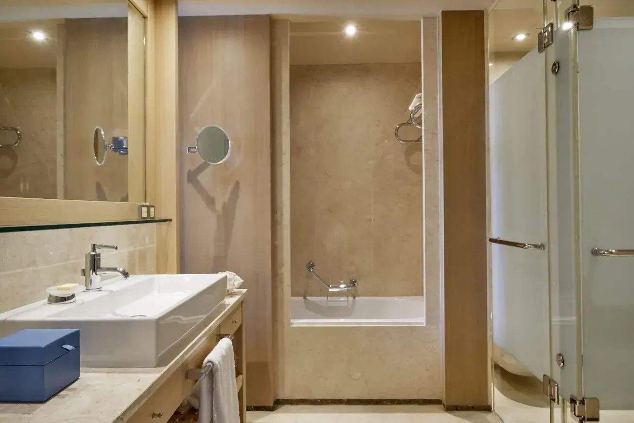 Helles gefliestes Badezimmer mit eingebauter Badewanne, gläserner Dusche und Holzwaschtisch.