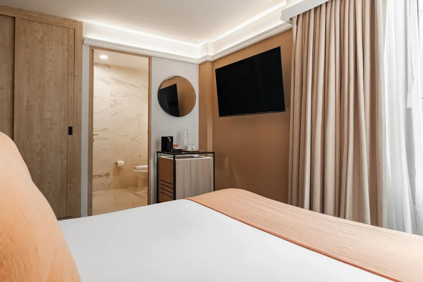 Bett in einem Hotelzimmer mit Wandfernseher und Blick auf das angrenzende Badezimmer.