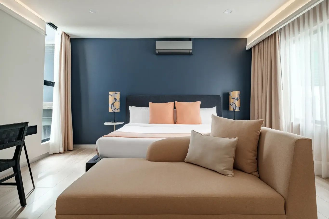 Schlafzimmer mit beige Liege im Vordergrund und einem großen Doppelbett an blauem Hintergrund.