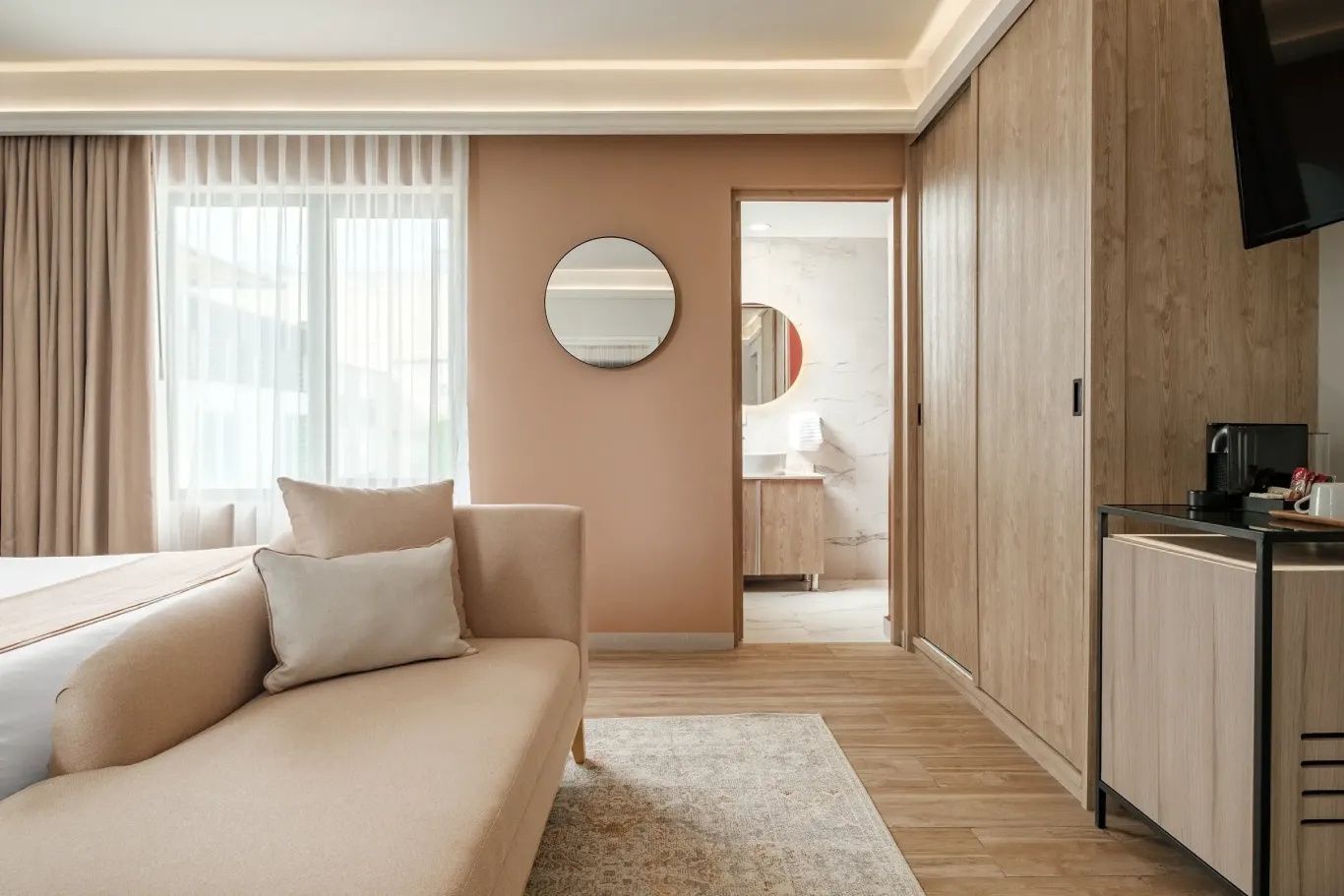 Wohnbereich mit hellbraunem Sofa, Spiegel an der Wand und Blick ins angrenzende Badezimmer.