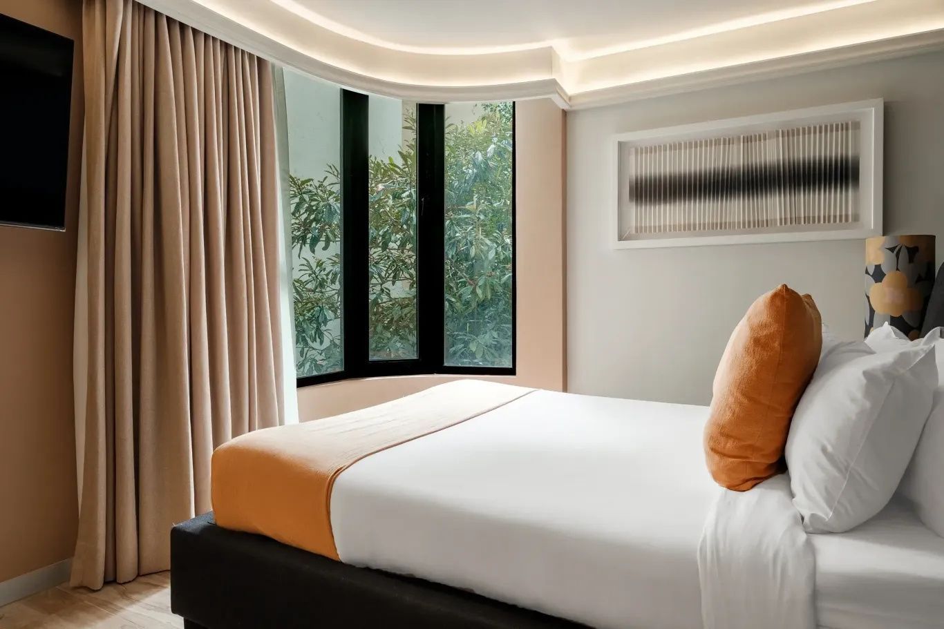 Blick über das Bett hin zu den Vorhängen und einem Fenster mit Sicht auf Bäume.