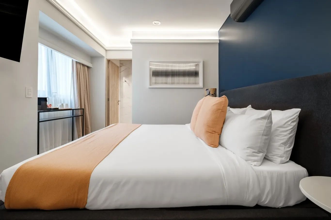 Doppelbett mit weißer Bettwäsche und pfirsichfarbenen Kissen in modernem Hotelzimmer.