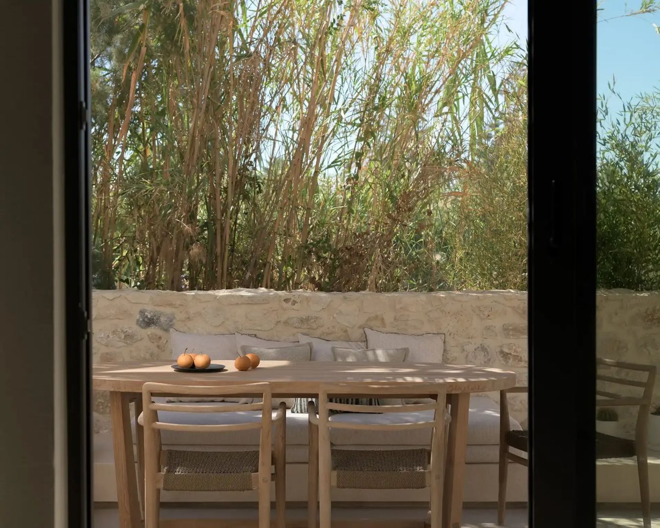 Holztisch mit Stühlen auf einer Terrasse, umgeben von dichten grünen Pflanzen.