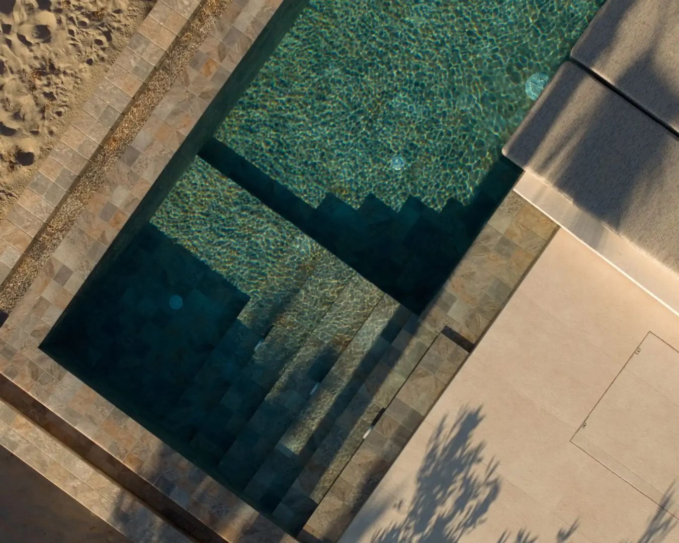 Draufsicht auf ein Schwimmbecken mit Unterwasserstufen und türkisblauem Wasser.