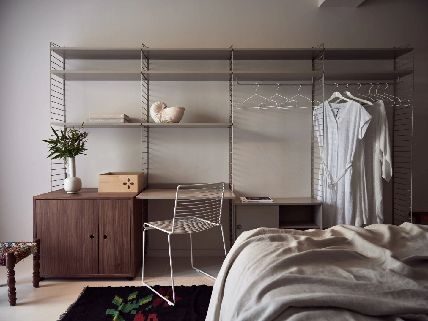 Arbeitsplatz und offenes Regalsystem aus Holz und Metall in einem Hotelzimmer.