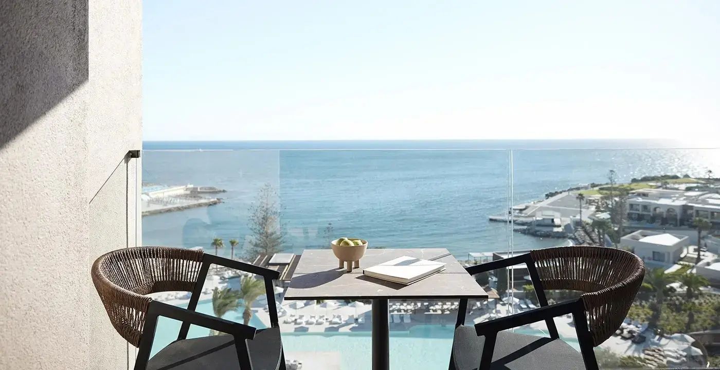 Balkon mit Tisch und Stühlen sowie Blick auf die Poolanlage und das Meer.
