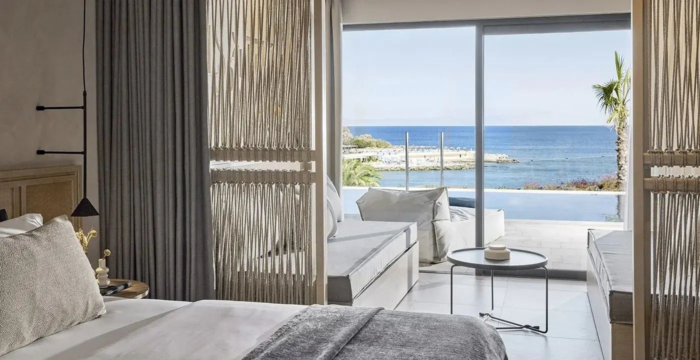 Modernes Hotelzimmer mit Raumteiler, Daybed und Terrasse mit Ausblick auf das Meer.