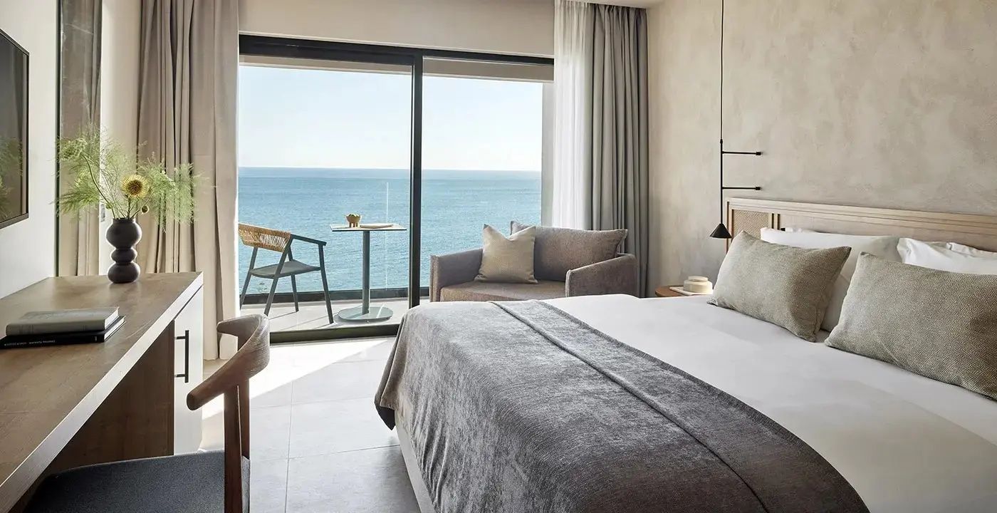 Doppelzimmer mit modernem Sessel und Balkon mit direktem Blick auf das blaue Meer.