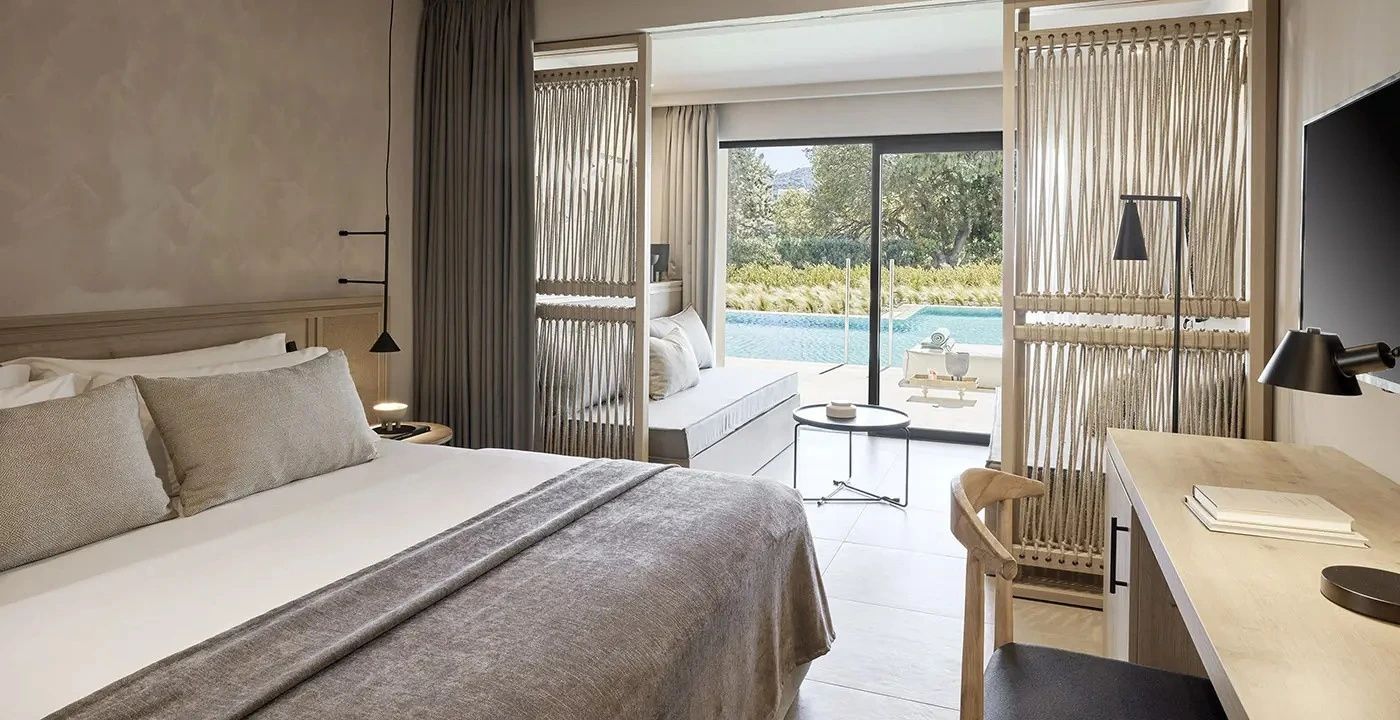 Helles Hotelzimmer mit Doppelbett, Sitzbereich und Zugang zur Terrasse mit Pool.