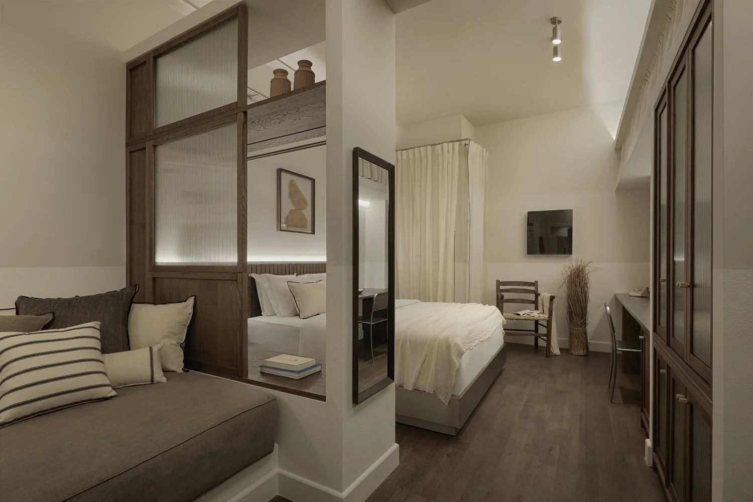 Offener Hotelraum mit Bett, Holztrenner und Sitzgelegenheit auf dunklem Holzboden.