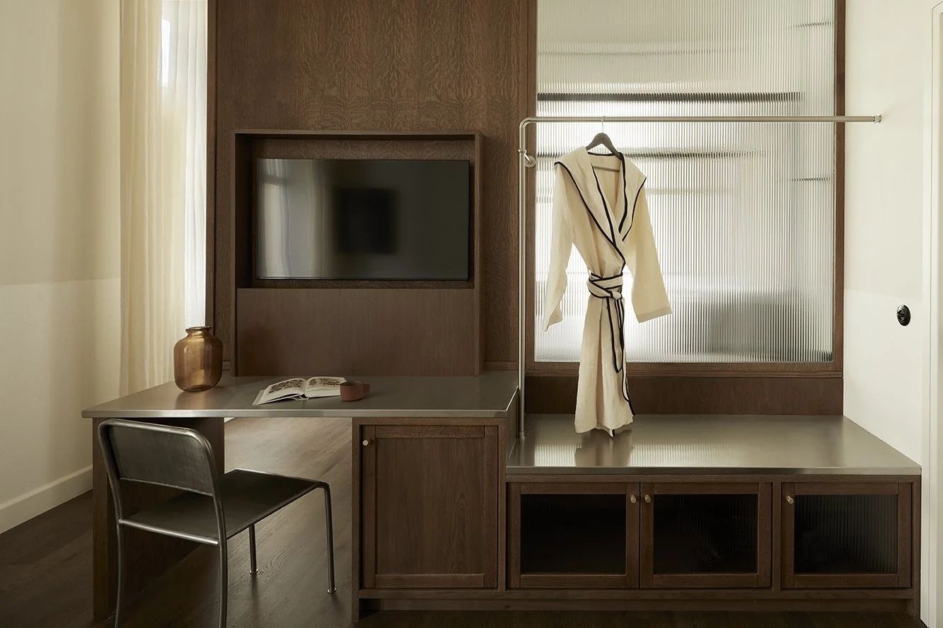 Hotelzimmer mit Holzverkleidung, Schreibtisch, Fernseher und aufgehängtem Bademantel.