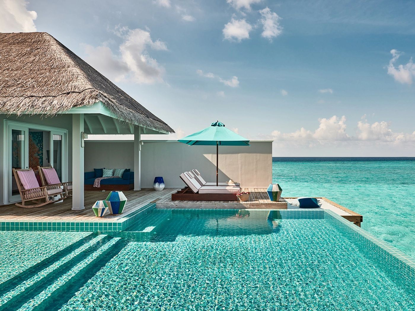Sonnendeck einer Wasservilla mit eigenem Infinity-Pool, Sonnenliegen und Blick auf das türkisblaue Meer.